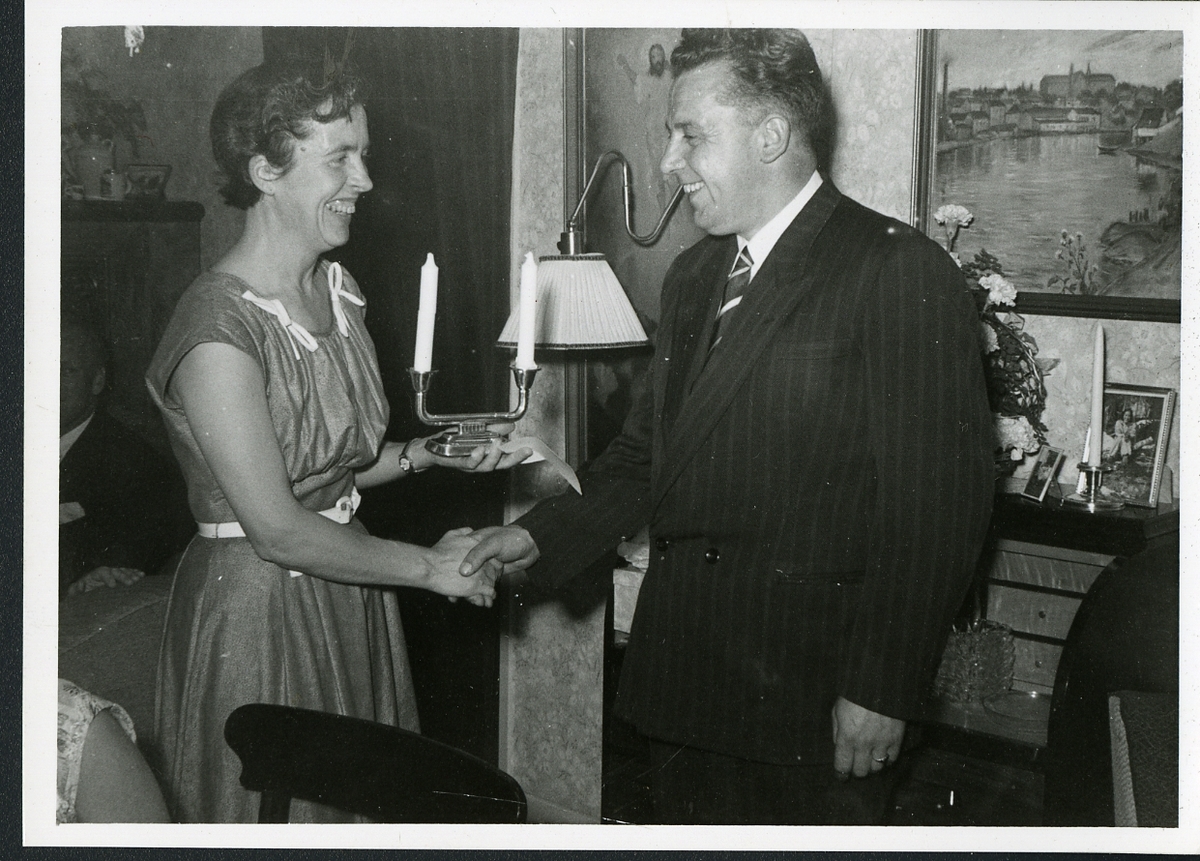 Ingeborg Ranum og Gudvar Olmar Lian, muligens hjemme hos Ingeborg, i forbindelse med "RE's 25- års jubileum- 1956" som det står bak fotografiet. RE står for Ranum Engros som ble stiftet i 1931, hvor Ingeborg Ranum var disponent fra 1942.