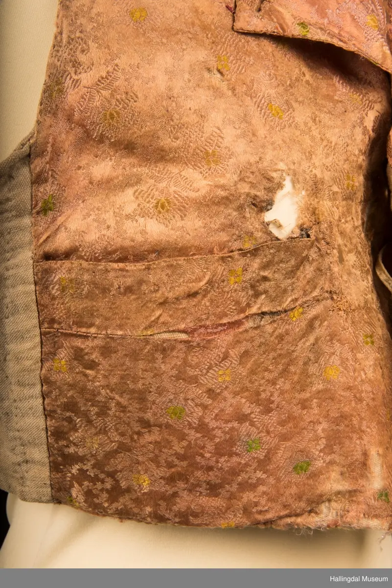 Opplysninger fra bunadsregistreringene i Flå:
"Halskragen og framstykkene er av jaquardvevet silke.  Brosjerte roser i gult og grønt på rosa bunn med lilla mønsterveving.  På framstykket er det 2 lommer, klaffene er 13 cm lange og 3 cm brede.  På hvert framstykke 4 knapphull + 1 på krageslaget.  4 sølvknapper på høyre sida, diam 1,2 cm. 1 knapp på hvert krageslag, 1 knapp på hver side øverst ved knappeslaget.  Knappene er gravert ornamentikk.  De 4 knappene er festa med et lysgrått band (lærreim) gjennom hempene på baksiden.  Bakstykket og foret er i heimevevd lin, også foret i framstykkene.  Ved kragen er det ei hempe.  Vesten er håndsydd.  17/10-1985 Marit Bergljot Jorde". Vesten hører sammen med fiskekjølkje HFN 13438.
