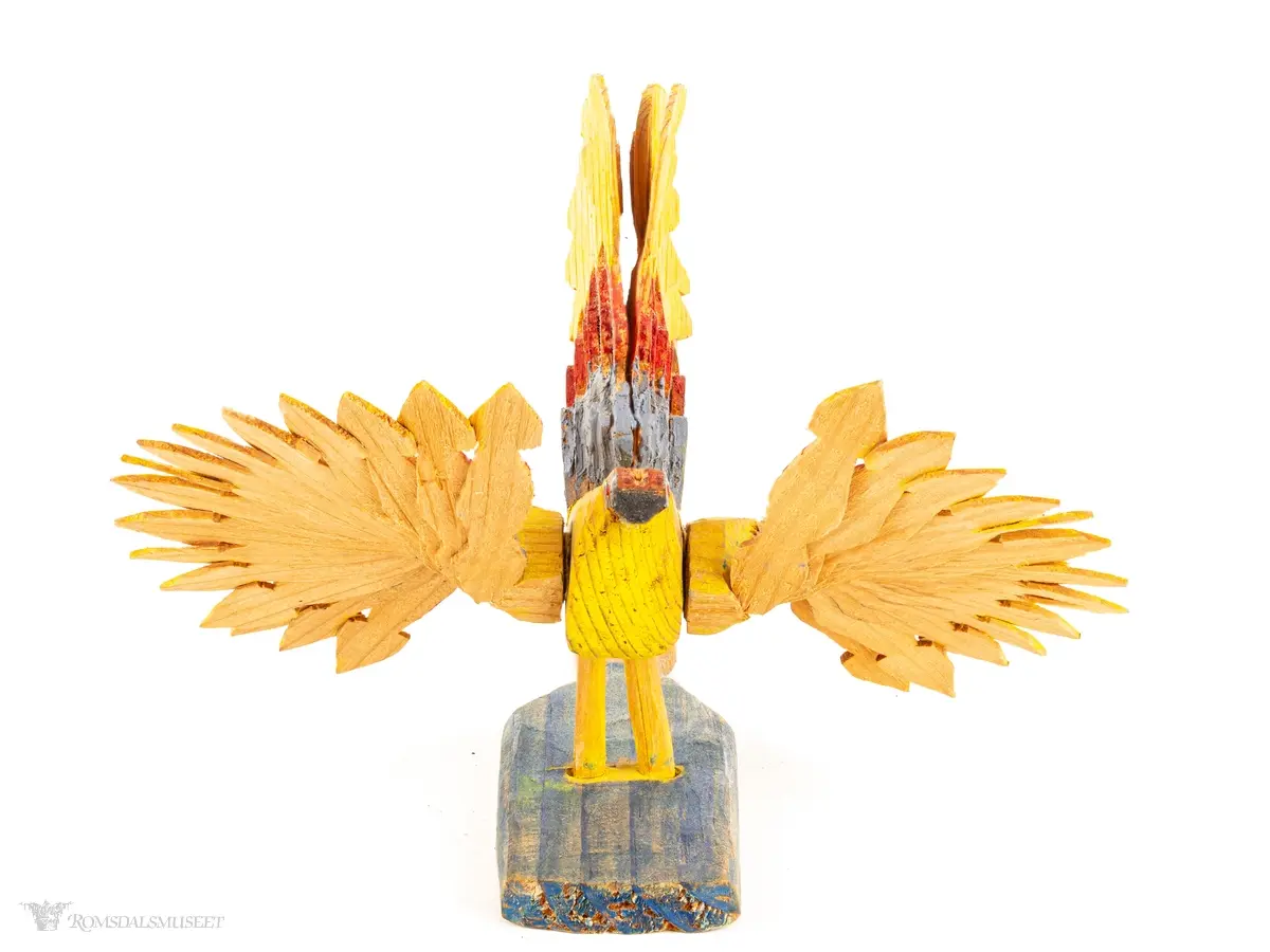 En sponfugl med livlige farger, med avtagbare vifteformede vinger, vifteformet hale og en avtagbar treplate med et lite håndtak. Kan være ment å være en liten vifte.