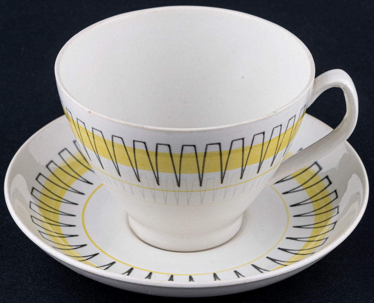 Kaffekopp med fat, modell BT i dekoren Palace, form och dekor av Berit Ternell. Svart stämpeldekor med gult band.