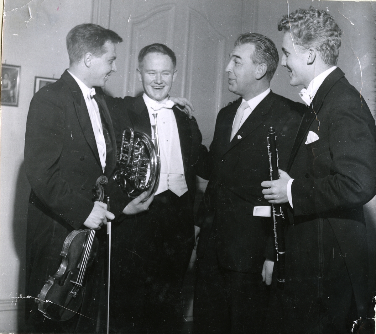 Gruppefotografi av tre musikere som står rundt Olaf Ranum. Fra venstre Arve Tellefsen på fiolin, Bjørn Fosdal på horn, Olaf Ranum og Brynjar Hoff på klarinett. Samlet i anledning butikkens 60-års jubileum.
08.12.1959.