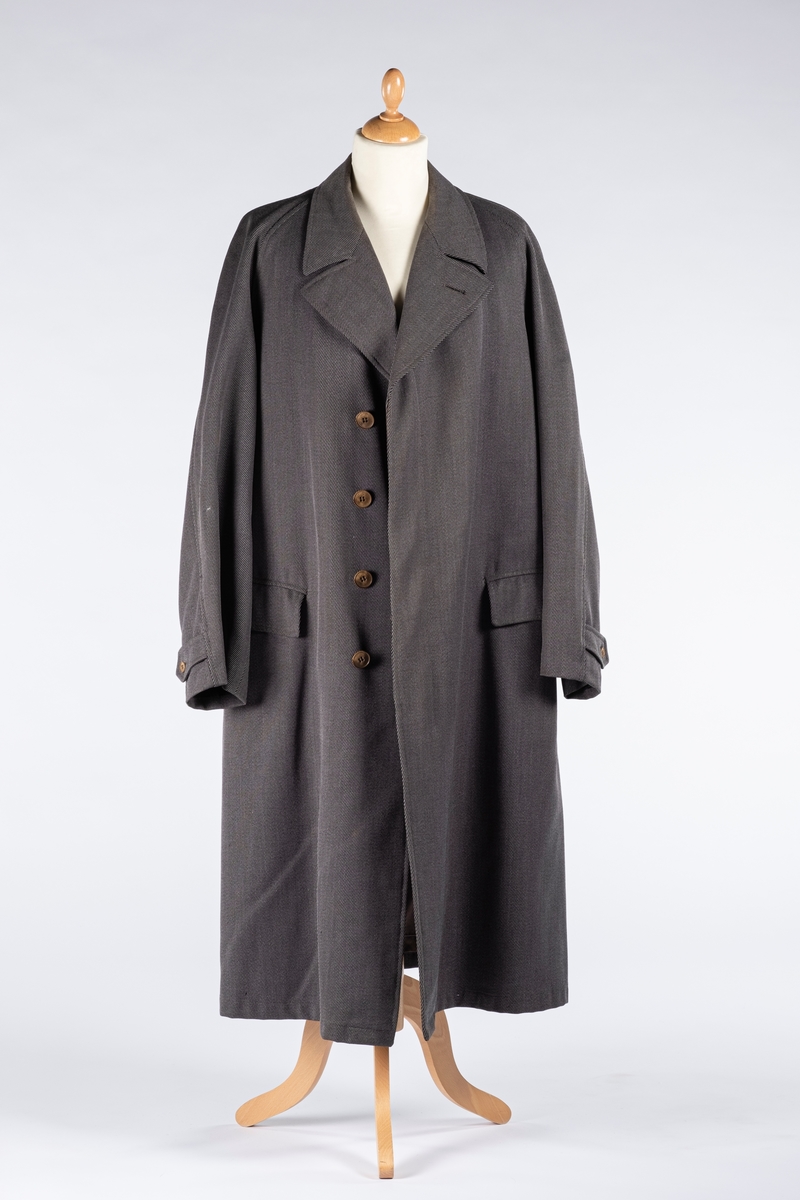 Rett frakk med slag og raglanerme. Foring av silke. Skjult knepping med fire knapper, kan også kneppe slaget under kragen. To lommer med klaff og to innerlommer. Splitt bak med knepping. Spensel nederst på ermene.