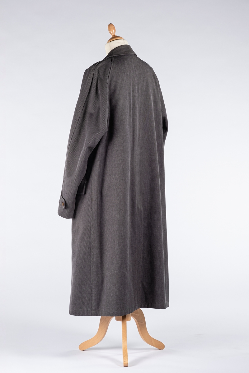 Rett frakk med slag og raglanerme. Foring av silke. Skjult knepping med fire knapper, kan også kneppe slaget under kragen. To lommer med klaff og to innerlommer. Splitt bak med knepping. Spensel nederst på ermene.