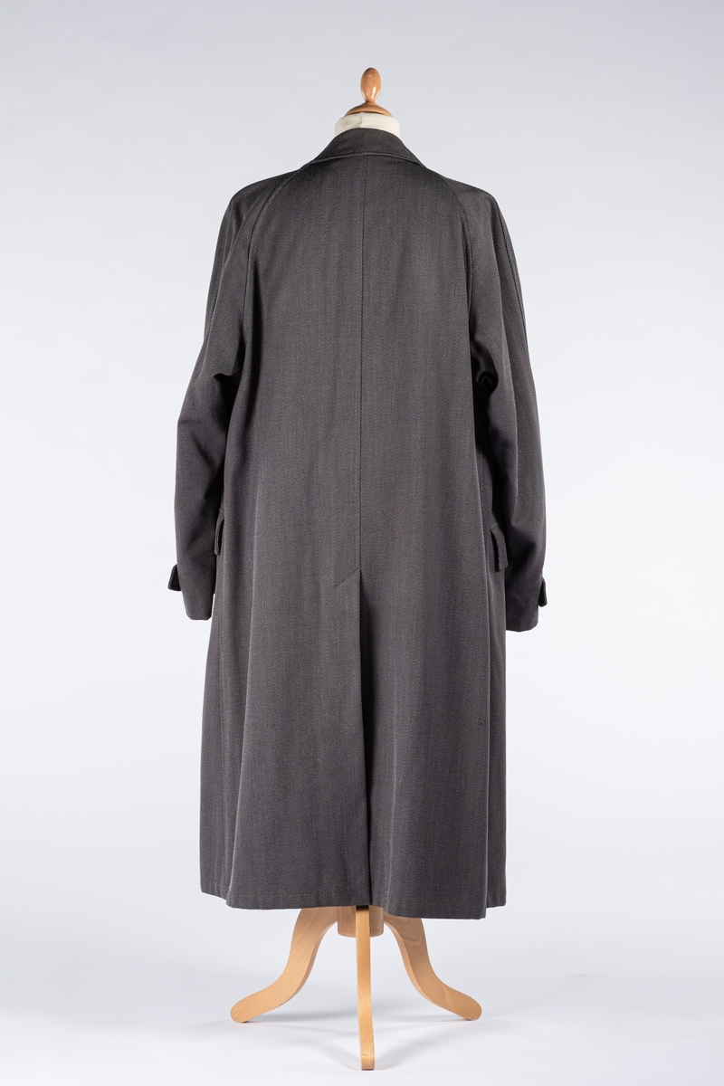 Rett frakk med slag og raglanerme. Foring av silke. Skjult knepping med fire knapper, kan også kneppe slaget under kragen. To lommer med klaff og to innerlommer. Splitt bak med knepping. Spensel nederst på ermene.