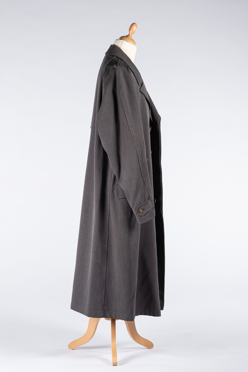 Rett frakk med slag og raglanerme. Foring av silke. Skjult knepping med fire knapper, kan også kneppe slaget under kragen. To lommer med klaff og to innerlommer. Splitt bak med knepping. Spensel nederst på ermene.