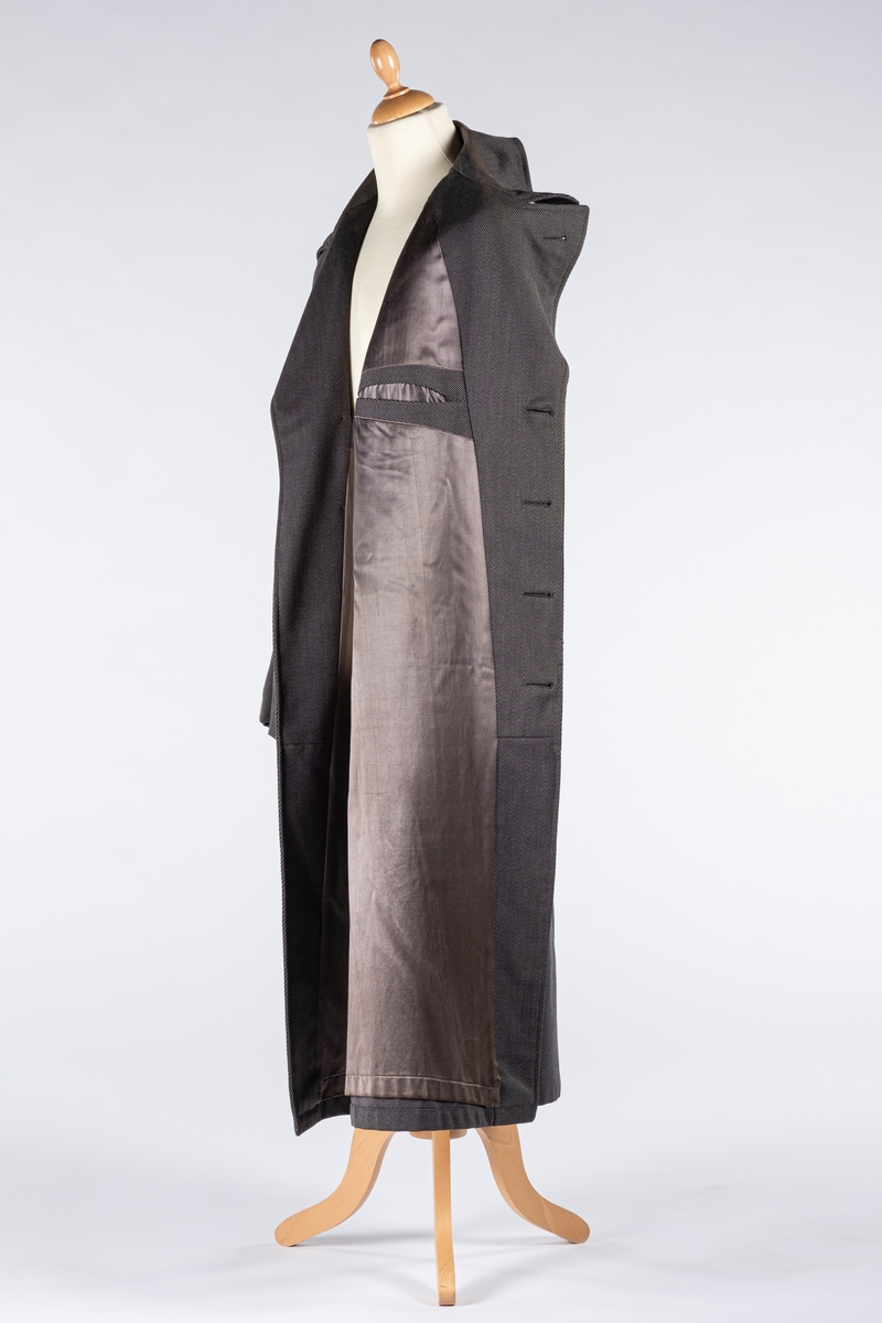 Rett frakk med slag og raglanerme. Foring av silke. Skjult knepping med fire knapper, kan også kneppe slaget under kragen. To lommer med klaff og to innerlommer. Splitt bak med knepping. Spensel nederst på ermene.