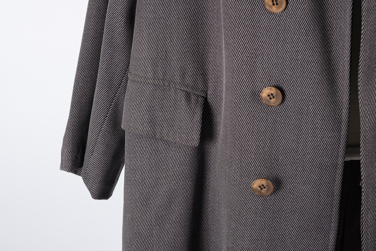 Rett frakk med slag og raglanerme. Foring av silke. Skjult knepping med fire knapper, kan også kneppe slaget under kragen. To lommer med klaff og to innerlommer. Splitt bak med knepping. Spensel nederst på ermene.