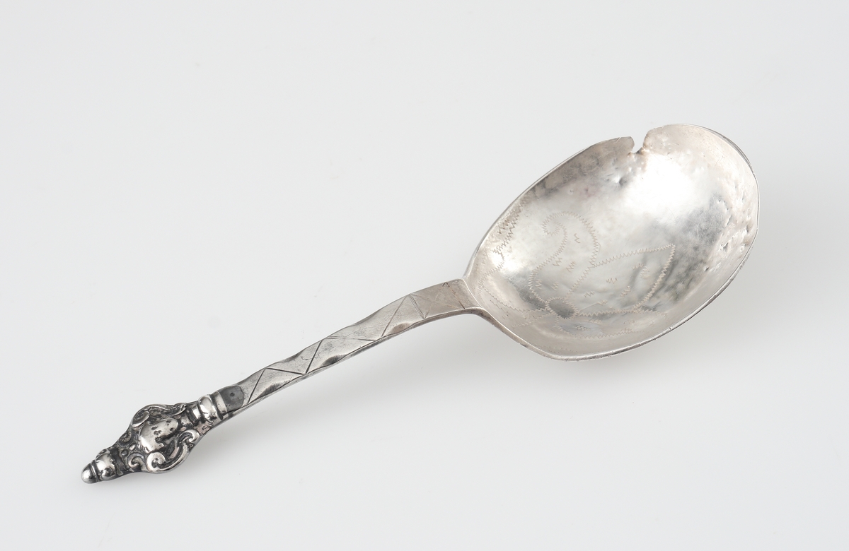 Brännvinssked av silver. 
S.k. kerubsked med kort, platt skaft, dekorerat med hålnät och zick-zackmönster. 
Skaftknopp bestående av ett enkelt (mycket nött) kerubhuvud. Bladet är ovalt med svisselerad blomdekor. 
Stämplar och åldermansranka på skaftets baksida.

Inskrivet i huvudbok 1870