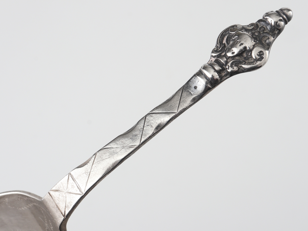 Brännvinssked av silver. 
S.k. kerubsked med kort, platt skaft, dekorerat med hålnät och zick-zackmönster. 
Skaftknopp bestående av ett enkelt (mycket nött) kerubhuvud. Bladet är ovalt med svisselerad blomdekor. 
Stämplar och åldermansranka på skaftets baksida.

Inskrivet i huvudbok 1870