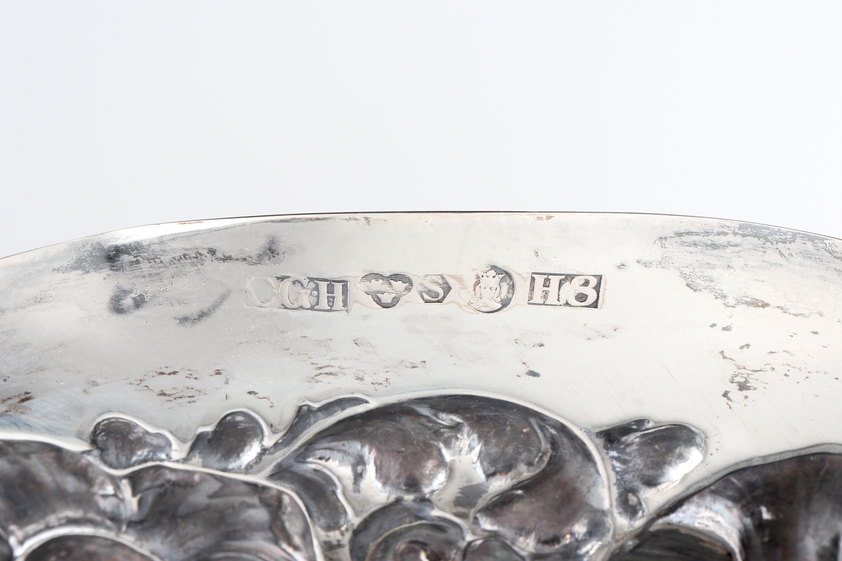 Fat av silver.
Ovalt prydnadsfat, med pressad dekor i hög relief på brättet, bestående av blommor och bladornament. Brättet är försett med två bekransade ramar, i den övre kanten är ett graverat monogram: "G B". I den undre kanten står: "19 22/12 35". På fatets baksida finns följande text: "Till Gunnar Borner på 50-årsdagen från kollegor i Kronobergs län". 
Stämplar på brättets undersida.

Inskrivet i huvudbok 1962