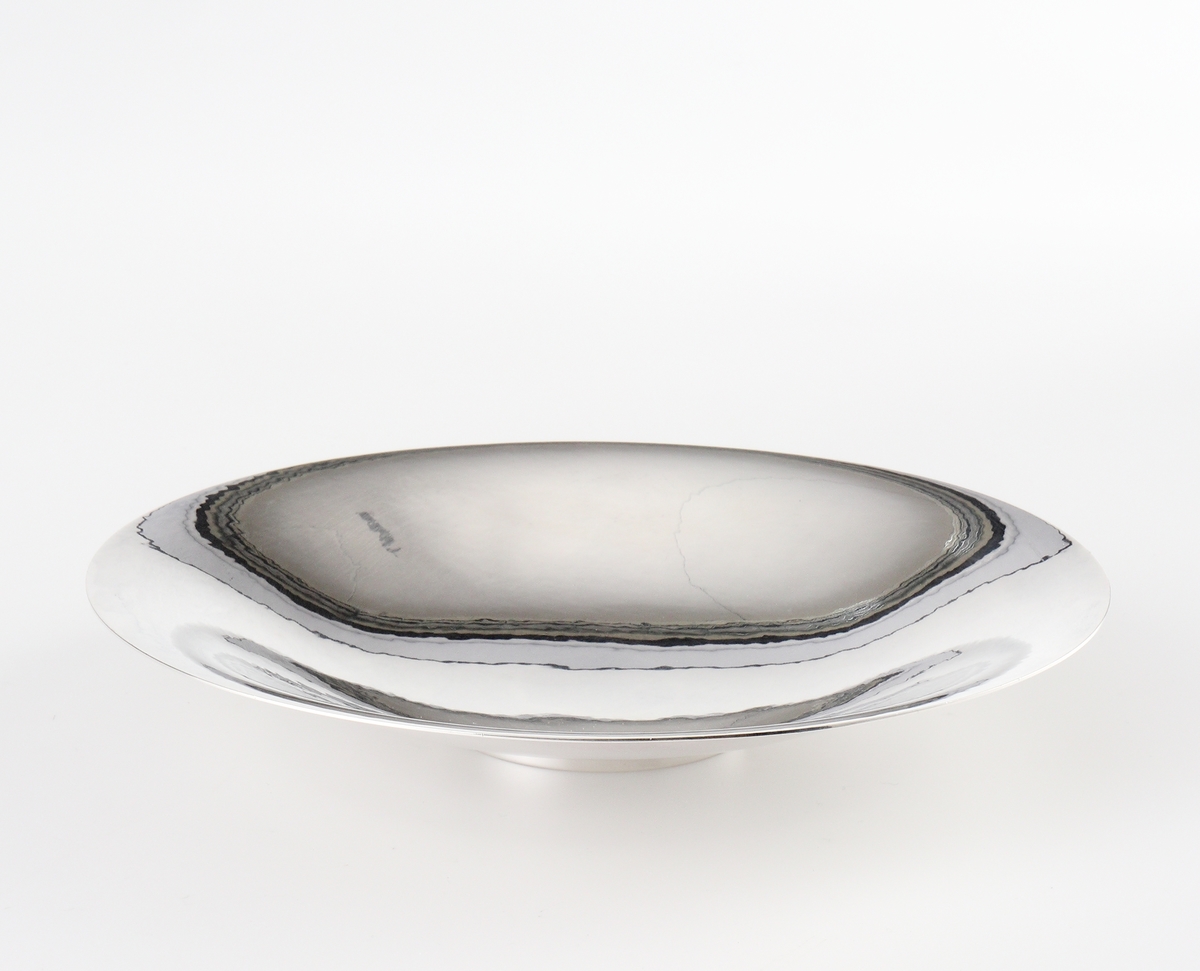 Fat av silver.
Rund, slät modell på låg, rund fot. På foten är graverat: "Fra Holmegaards Glasverk 8-9-1962". 
Inuti foten finns tillverkarstämpel m.m.

Inskrivet i huvudbok 1983.