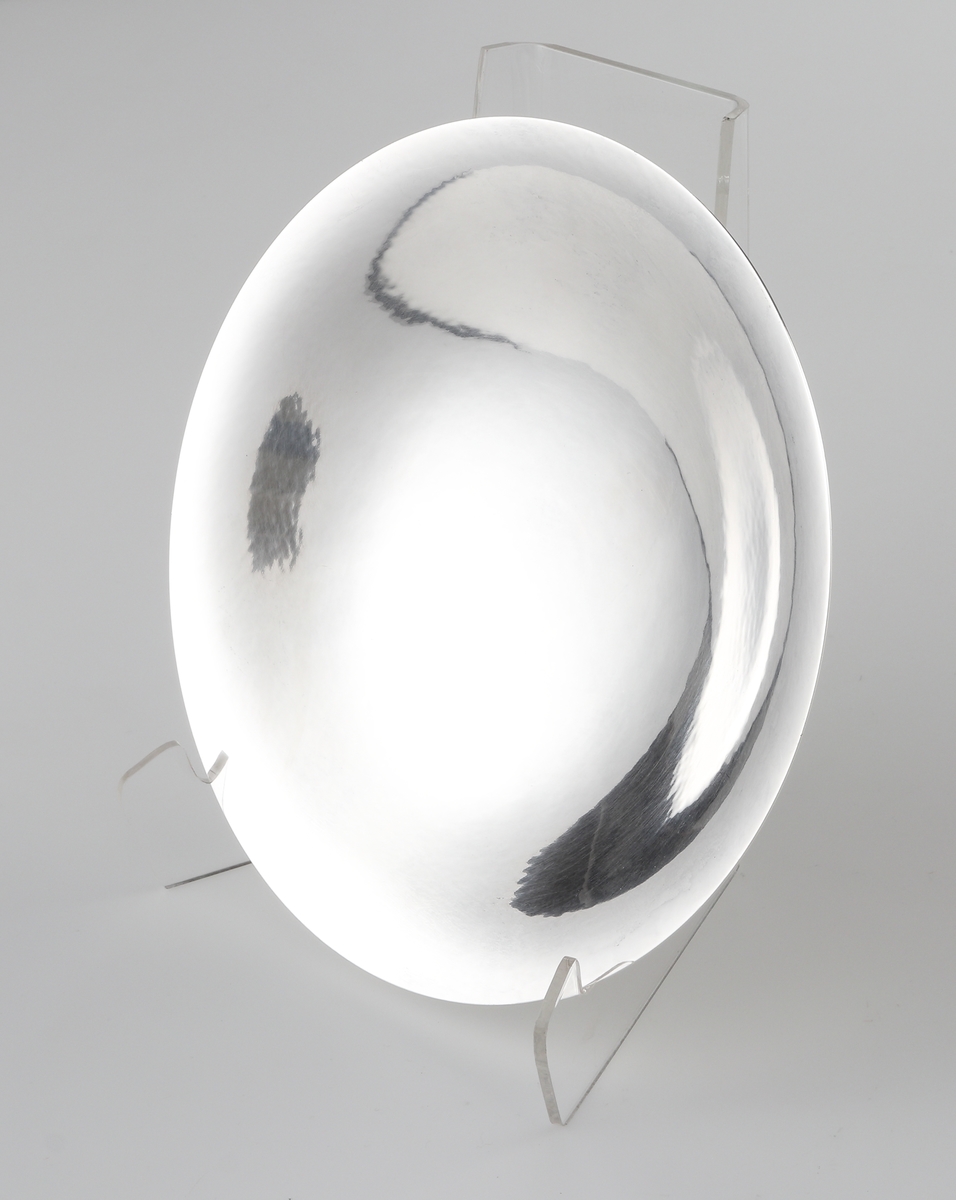 Fat av silver.
Rund, slät modell på låg, rund fot. På foten är graverat: "Fra Holmegaards Glasverk 8-9-1962". 
Inuti foten finns tillverkarstämpel m.m.

Inskrivet i huvudbok 1983.