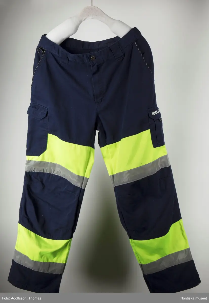 Mörkblå byxor som hör till arbetskläder för gruvarbete, tillverkade av  polyester (80%) och bomull (20%) med reflexband och varningsfärgat neongult tyg av polyester (65%) och bomull (35%). Till skyddsdräkten hör även en jacka. Plaggen är tillverkade av Grolls AB, märkta Björnkläder, EN 471. Med metallknappar, blixtlås och fickor (6 st).