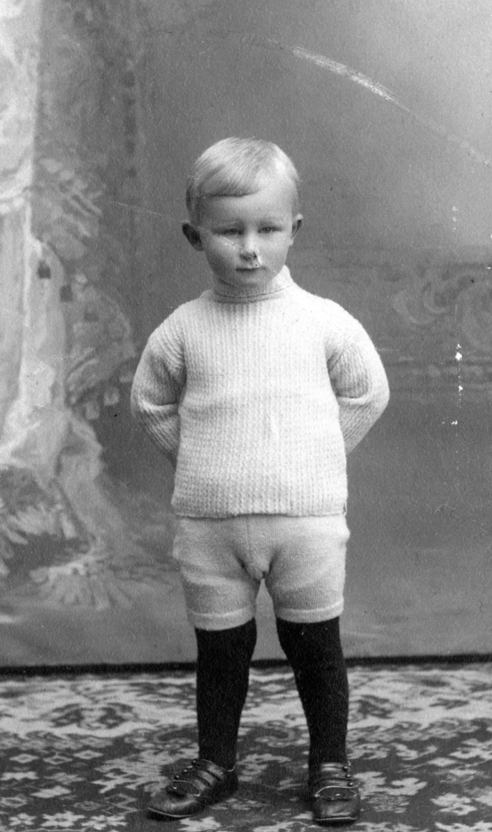 Thor Thorsen i hvit strikket genser og knickers, hender på ryggen. Sønn av Kitty og Christen Thorsen.