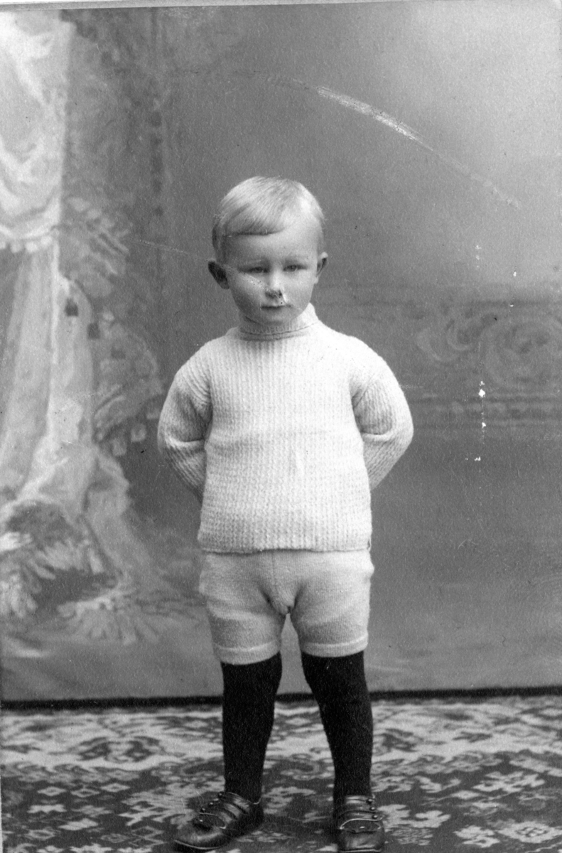 Thor Thorsen i hvit strikket genser og knickers, hender på ryggen. Sønn av Kitty og Christen Thorsen.