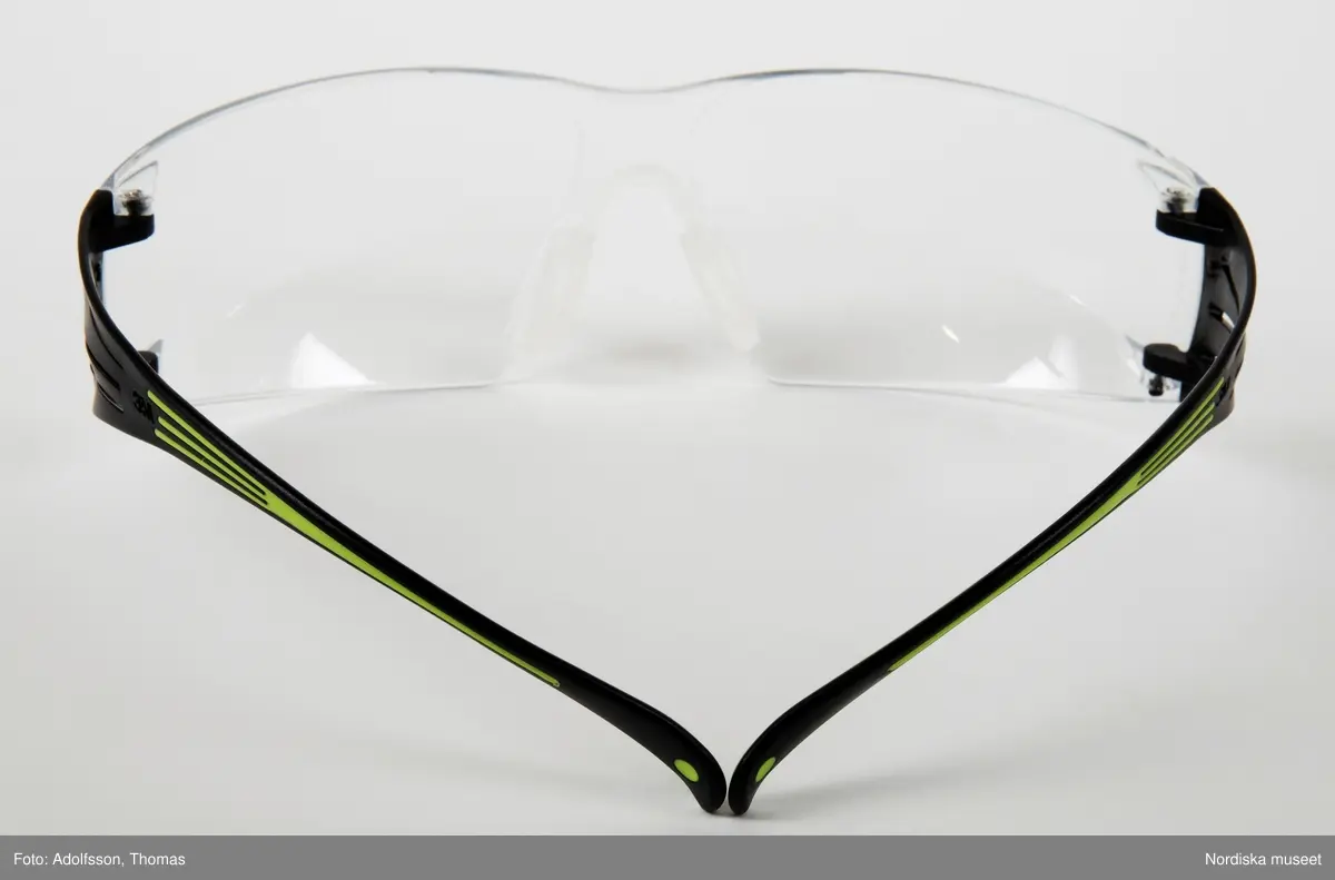 Skyddsglasögon av genomskinlig plast, med mjuka skalmar i svart och grönt. Används för att skydda ögonen mot damm och smuts. Enligt bruksanvisningen uppfyller de grundläggande säkerhetskrav i EN166. Tillverkare: 3M United Kingdom, Cain Road, Bracknell. Märkning: SF 400 Series.
