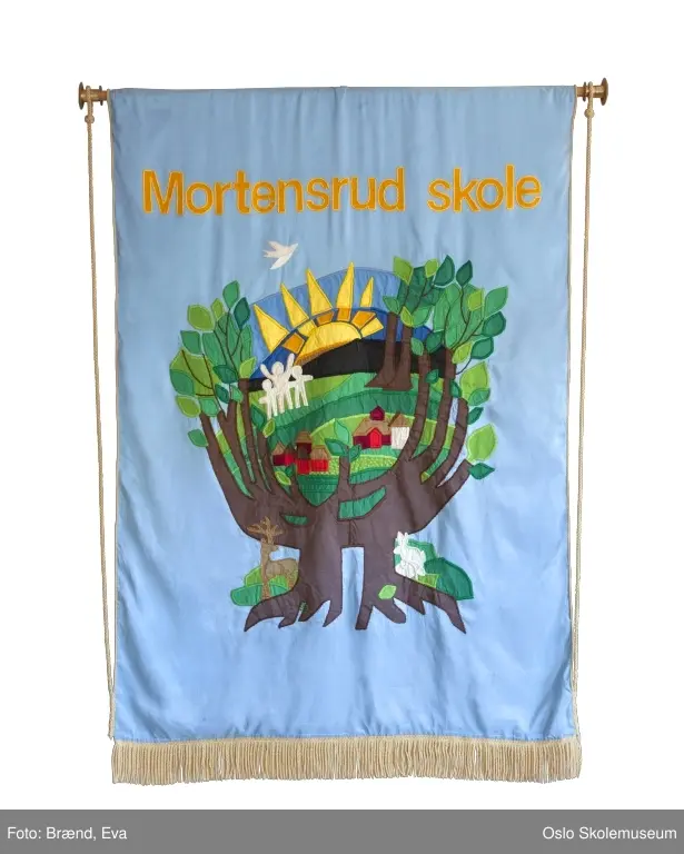 Nyere fane: Landskap med skolens egne bygninger og skogen rundt på blå bakgrunn. Stiliserte barn og dyr samte en stor gul sol. Øverst på fanen står skolens navn. 

Eldre fane: Landskap med skolens egene bygninger og skogen rundt på rød bakgrunn. Stil og formspråk hentet fra folkeeventyrene. Øverst på fanen står skolens navn.