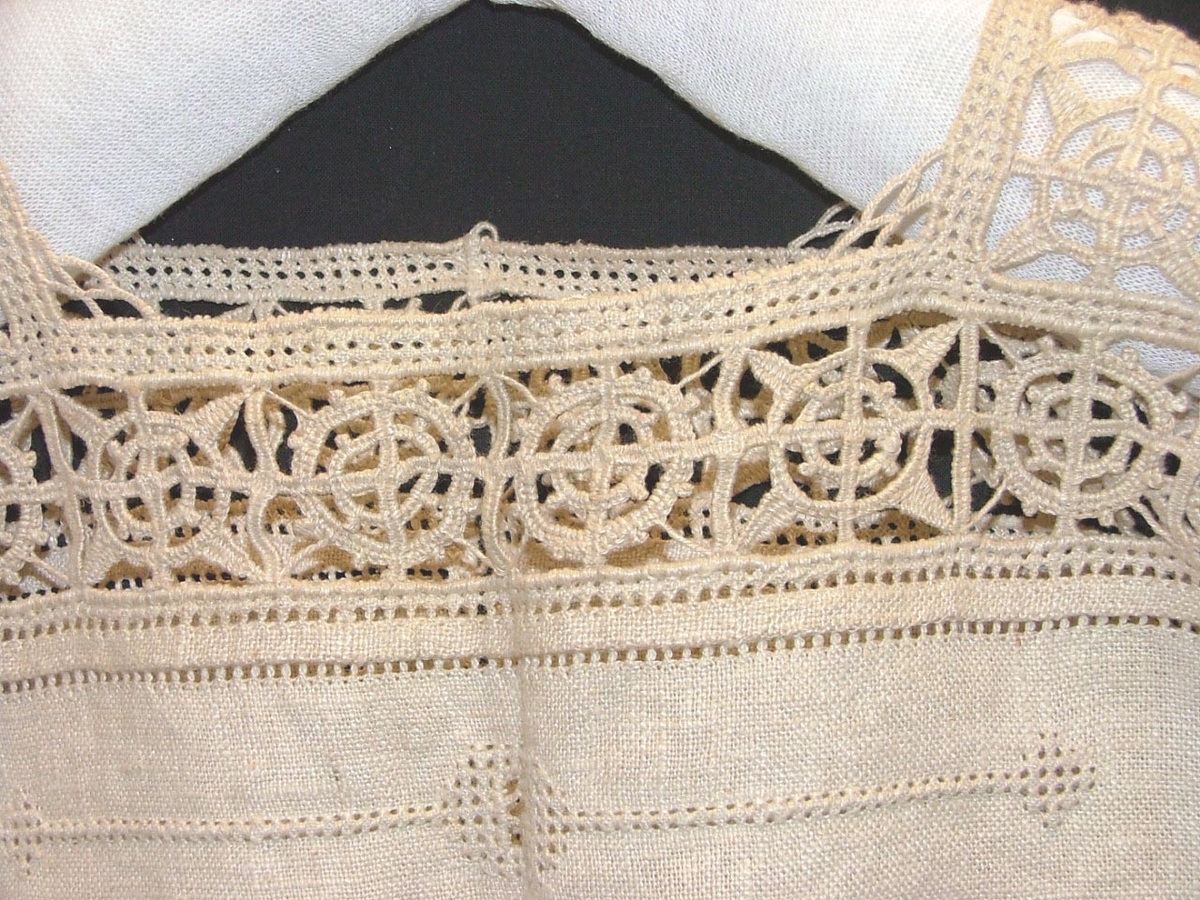 Av grov halvblekt linnelärft, två framstycken, ett bakstycke, besparing, korta ärmar skurna i ett med ovanstående stycken, bårder i spetssöm med grovt halvblekt lingarn kring besparing, hals och på ärmarna, samt hopdragssöm, s.k. myrgång, kring alla kanter samt på ryggstycket, i framkanten åtta sydda tränsar, knappar saknas, blusen rynkad mot smal midjelinning.

Tråckeltråd kvar i midjelinningen, knappar ej isydda.