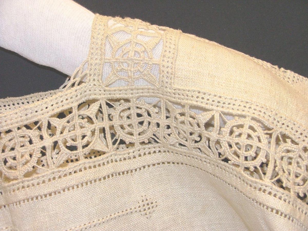 Av grov halvblekt linnelärft, två framstycken, ett bakstycke, besparing, korta ärmar skurna i ett med ovanstående stycken, bårder i spetssöm med grovt halvblekt lingarn kring besparing, hals och på ärmarna, samt hopdragssöm, s.k. myrgång, kring alla kanter samt på ryggstycket, i framkanten åtta sydda tränsar, knappar saknas, blusen rynkad mot smal midjelinning.

Tråckeltråd kvar i midjelinningen, knappar ej isydda.