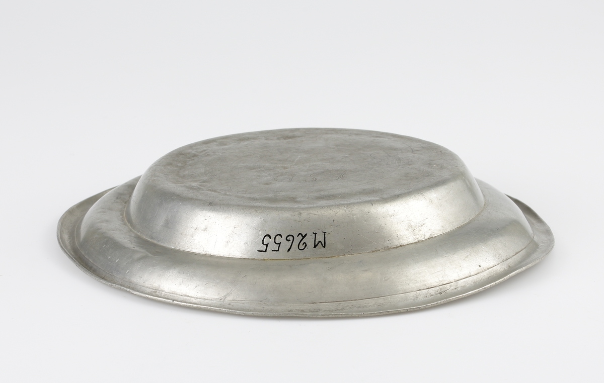 Fat av tenn. Rund, djup modell med uppsvängd bräm, dekorerad med en svarvad linje. 
Ägarinitialer på bottnens utsida: "LSD". Stämplar (mycket nötta och svårtydda) i fatets spegel.

Inskrivet i huvudbok 1903.