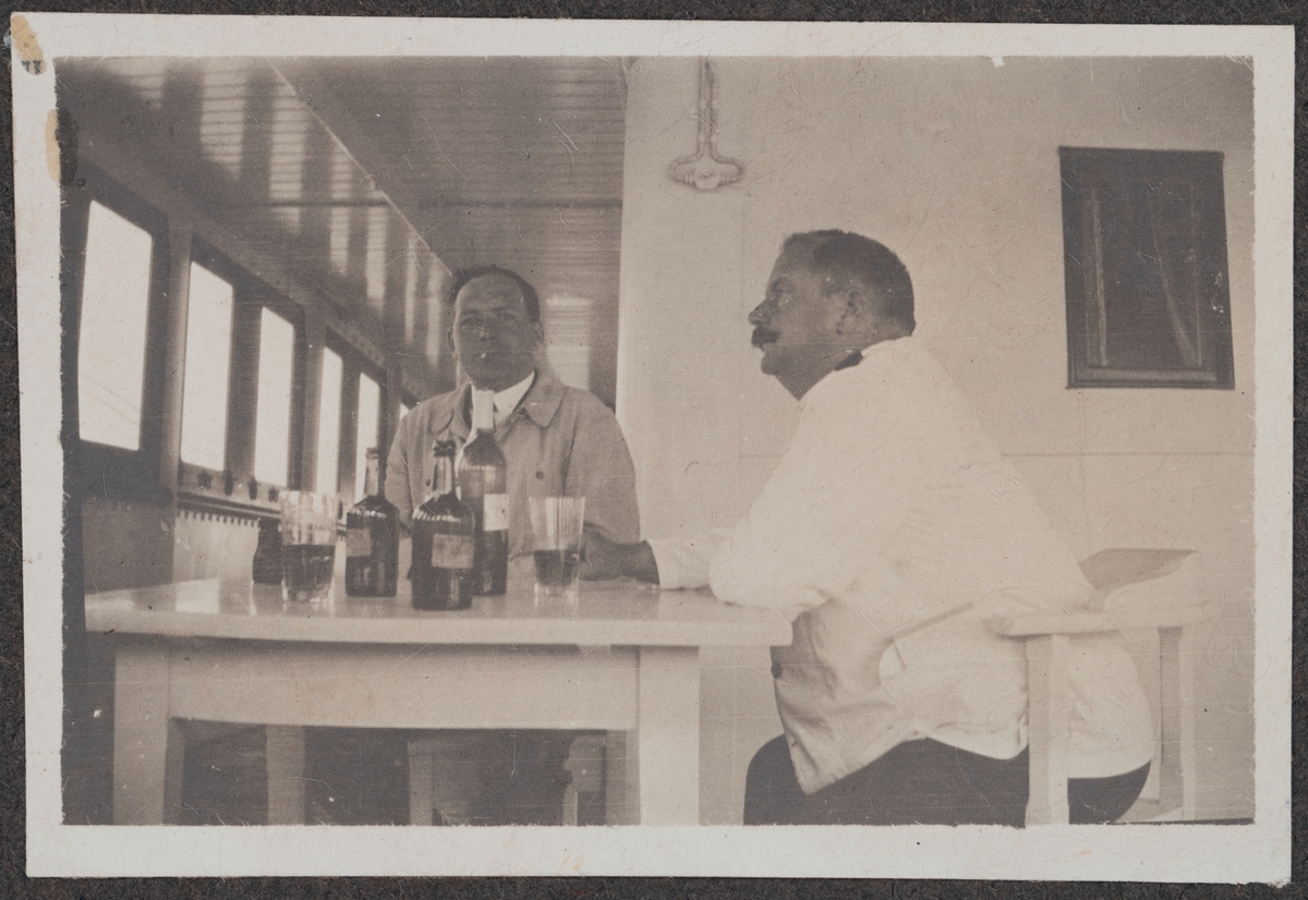 En okänd herre (möjligen Vilhelm Quiding) och kapten Frans Wilhelm Grundberg som sitter vid ett bord och förtär någon form av alkohol.
Bildtext: "Vila vid denna källa."