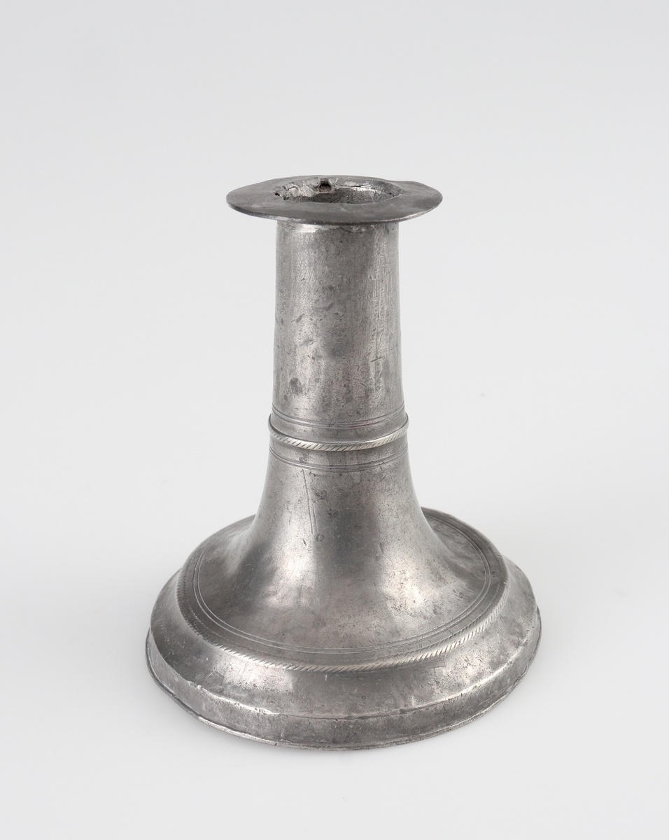 Ljusstake (2 st.) av tenn. 
Konisk ljuspipa med fast manschett. Låg klockfot, den ena med graverad bård. 
Stämplar (delvis otydliga) på fotens yttre nedre kant.

Inskrivet i huvudbok 1934.