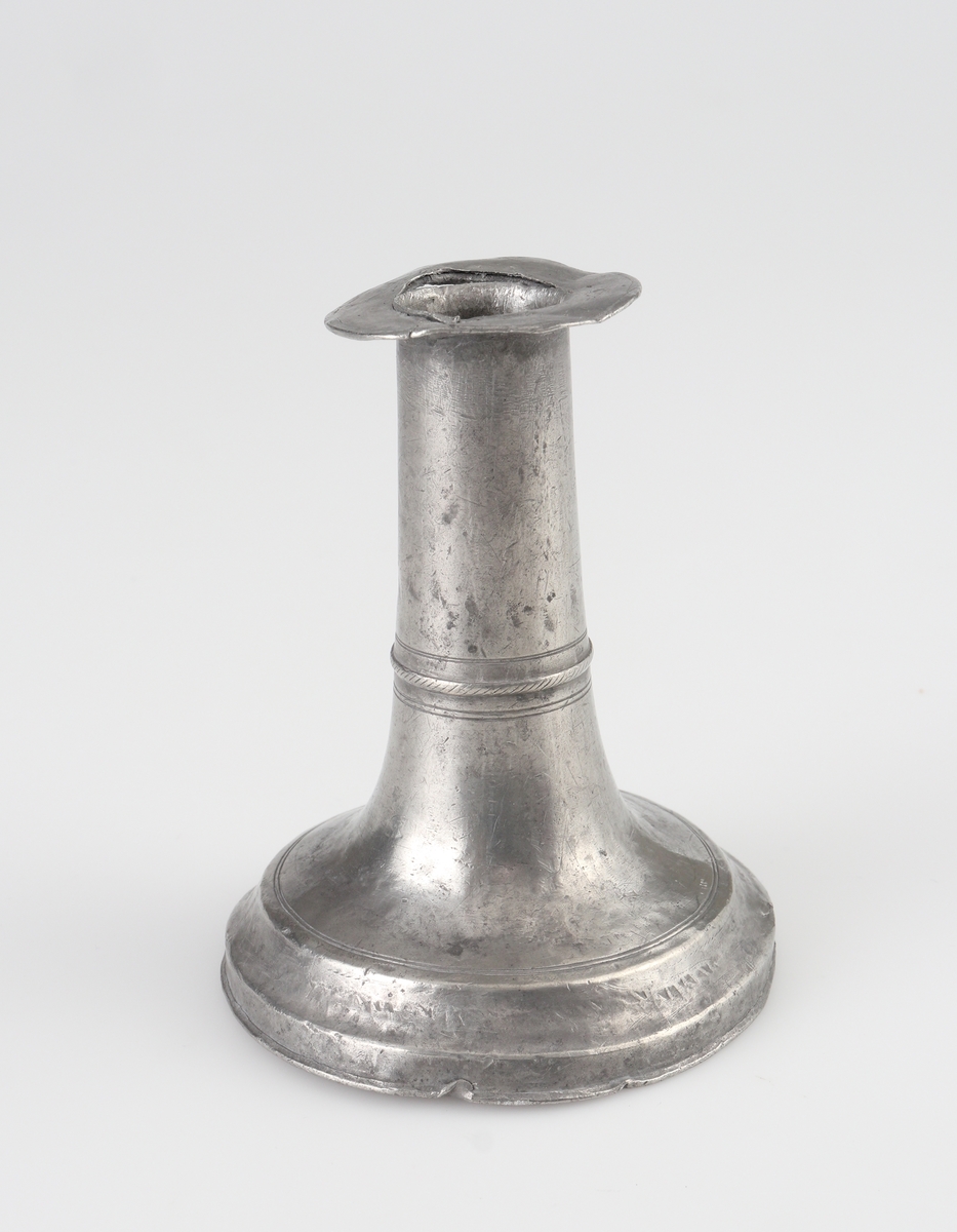 Ljusstake (2 st.) av tenn. 
Konisk ljuspipa med fast manschett. Låg klockfot, den ena med graverad bård. 
Stämplar (delvis otydliga) på fotens yttre nedre kant.

Inskrivet i huvudbok 1934.