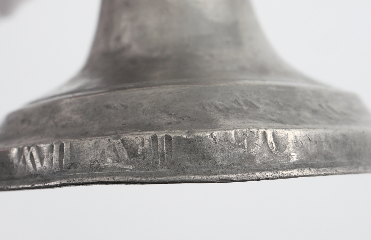 Ljusstake (2 st.) av tenn. 
Konisk ljuspipa med fast manschett. Låg klockfot, den ena med graverad bård. 
Stämplar (delvis otydliga) på fotens yttre nedre kant.

Inskrivet i huvudbok 1934.