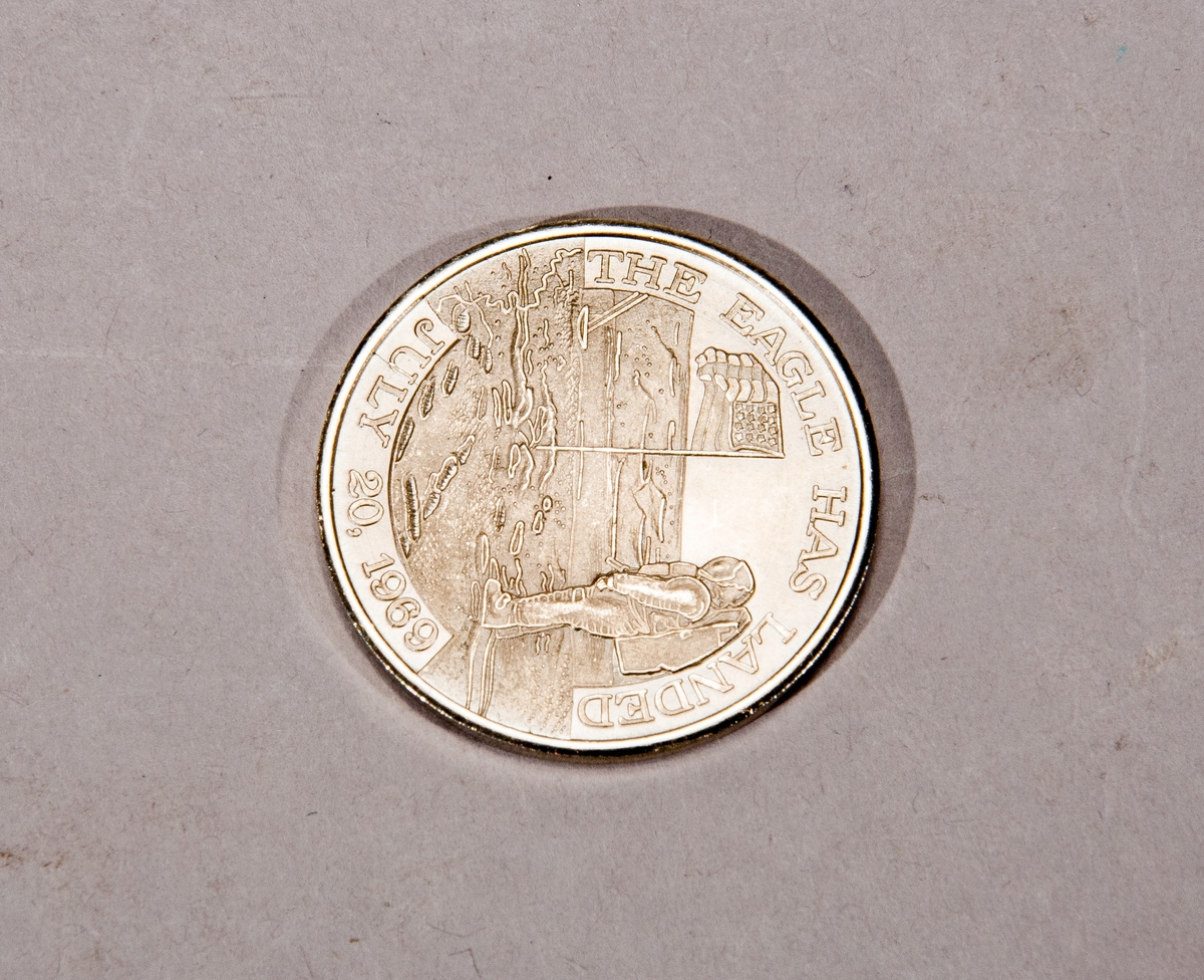 Åtsidan: Astronaut vid amerikanska flaggan vid den första månlandningen, text runtom: "The Eagle has landed July 20 1969". Baksida: "This medallion contains metal from spacecrafts Columbia and Eagle that took astronauts Armstrong Aldrin and Collins on their historic Apollo 11 mission that resulted in the first landing of man on the moon".