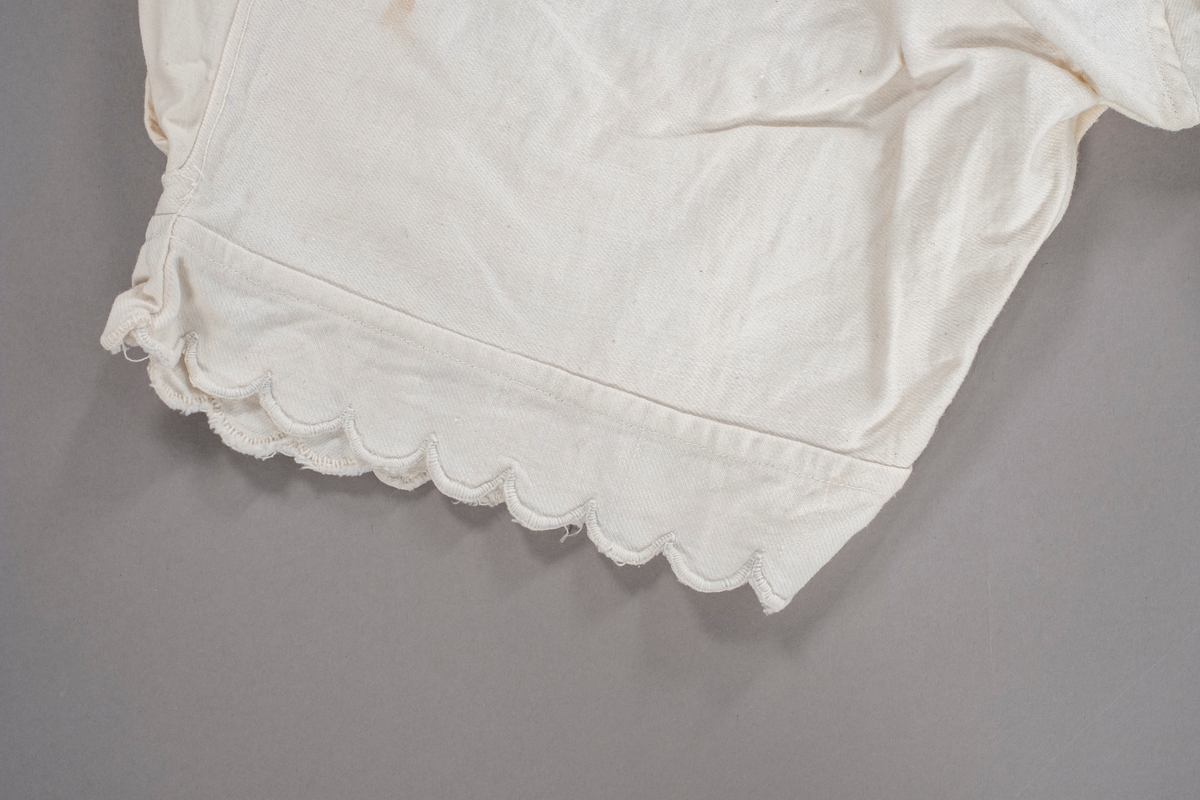 Knekort underbukse med tungekant nederst. Den har åpning i sidene som lukkes med knapper.  Den er utvidet i livet ved innfelling av tøystykker. I front er det brodert initialer.