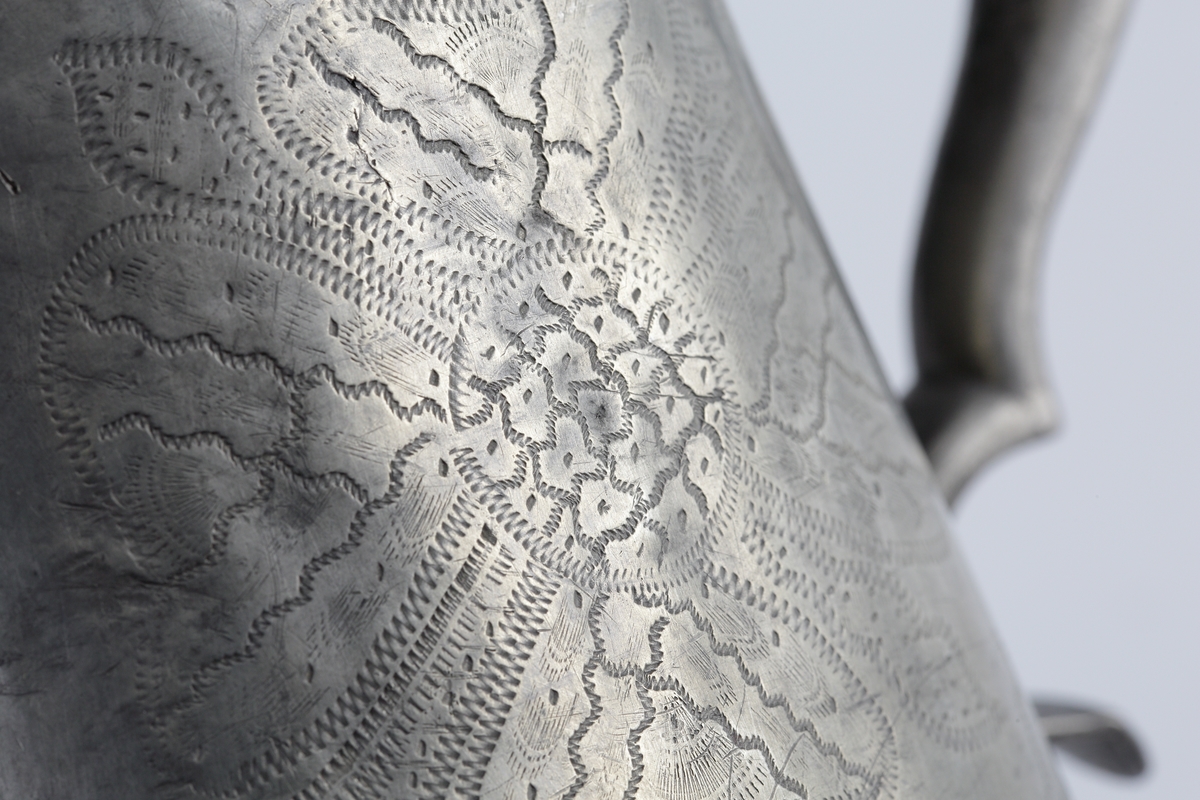 Stop av tenn.
Konisk modell. Svängd hänkel och tumgreppsknopp. Svängd, fasetterad snås. Fräcklad blomdekor på livet. På locket medaljong med Oscar I:s bild och inskriptionen: "Oscar, Sveriges och Norges konung". Stämplar på bottnens insida.

Inskrivet i huvudbok 1955.