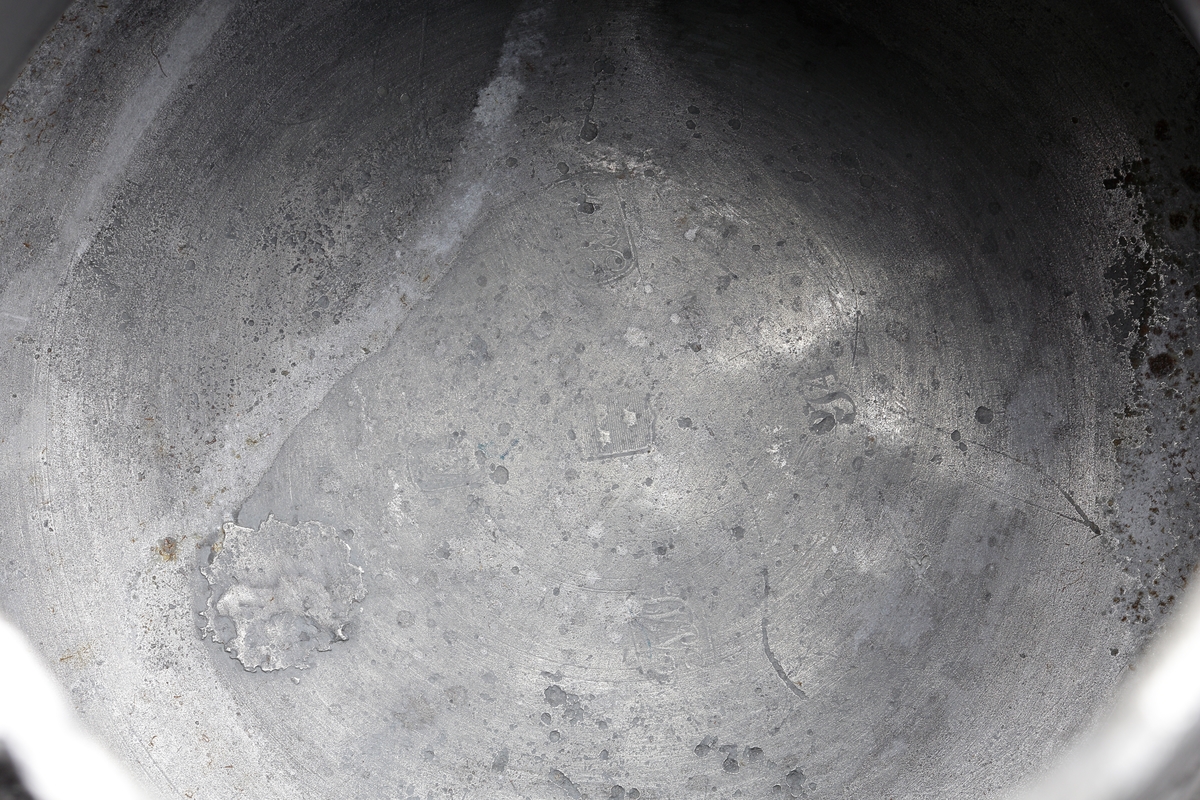 Stop av tenn.
Konisk modell. Svängd hänkel och tumgreppsknopp. Svängd, fasetterad snås. Fräcklad blomdekor på livet. På locket medaljong med Oscar I:s bild och inskriptionen: "Oscar, Sveriges och Norges konung". Stämplar på bottnens insida.

Inskrivet i huvudbok 1955.