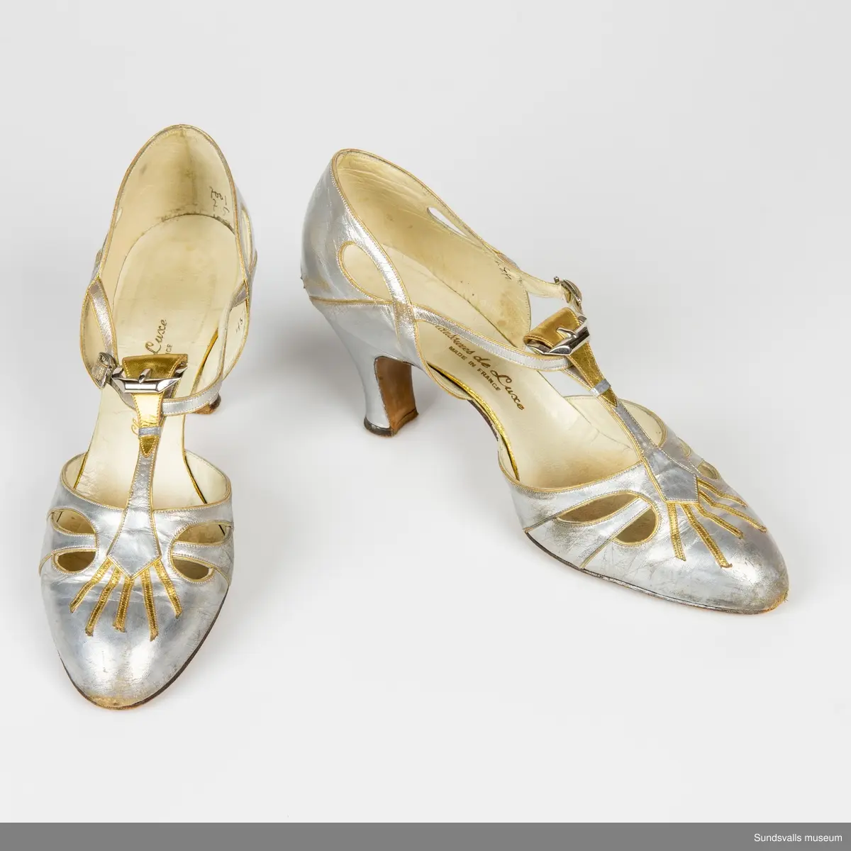 Ett par silverfärgade damskor med gulddekoration. Sleif, hög smal klack. Märkning 'Chaussures de Luxe Made in France'.