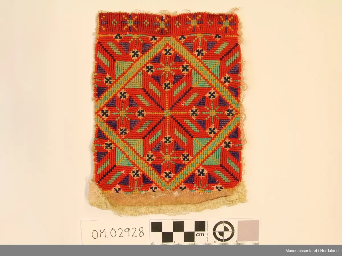 Rektangulær bringeduk med "enkel" og dobbel kross-sting i forskjellige retningar. Stor åttebladrose i midten og fire små oppe, nede og på sidene med ei rame rundt. I kvart hjørne er det eit blad av åttebladrose. Bord oppe med anna mønster (slags stjernemønster).  Raud hovudfarge. Dei mørkeblå krossane er sydd med kross-sting. Fargane er litt falma, spesielt den grønturkise og gule.