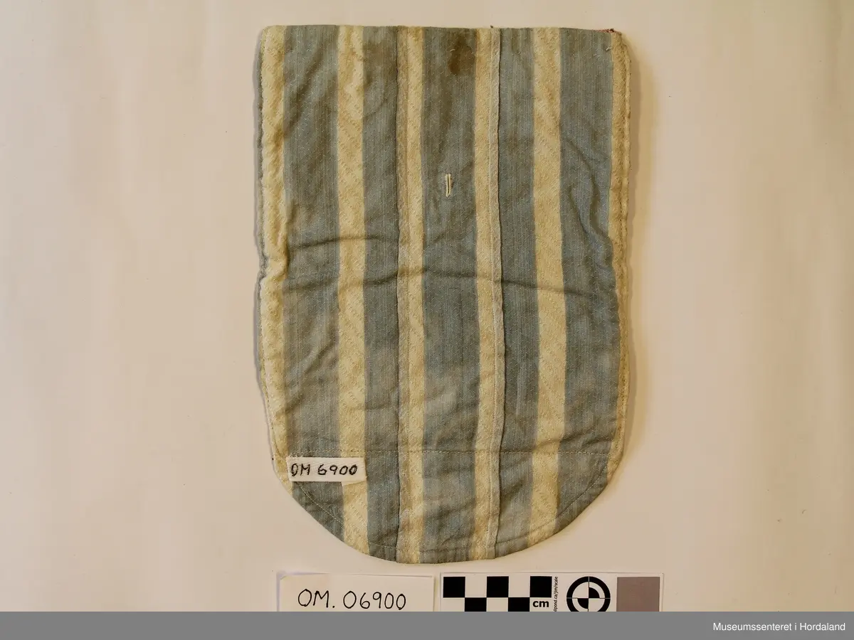 Brodert brystduk i repeterande mønster med sikksakk-border. Broderiet er rektangulært, bakstykket endar i ein halvrunding nedom broderiet. Stripete stoff på baksida.