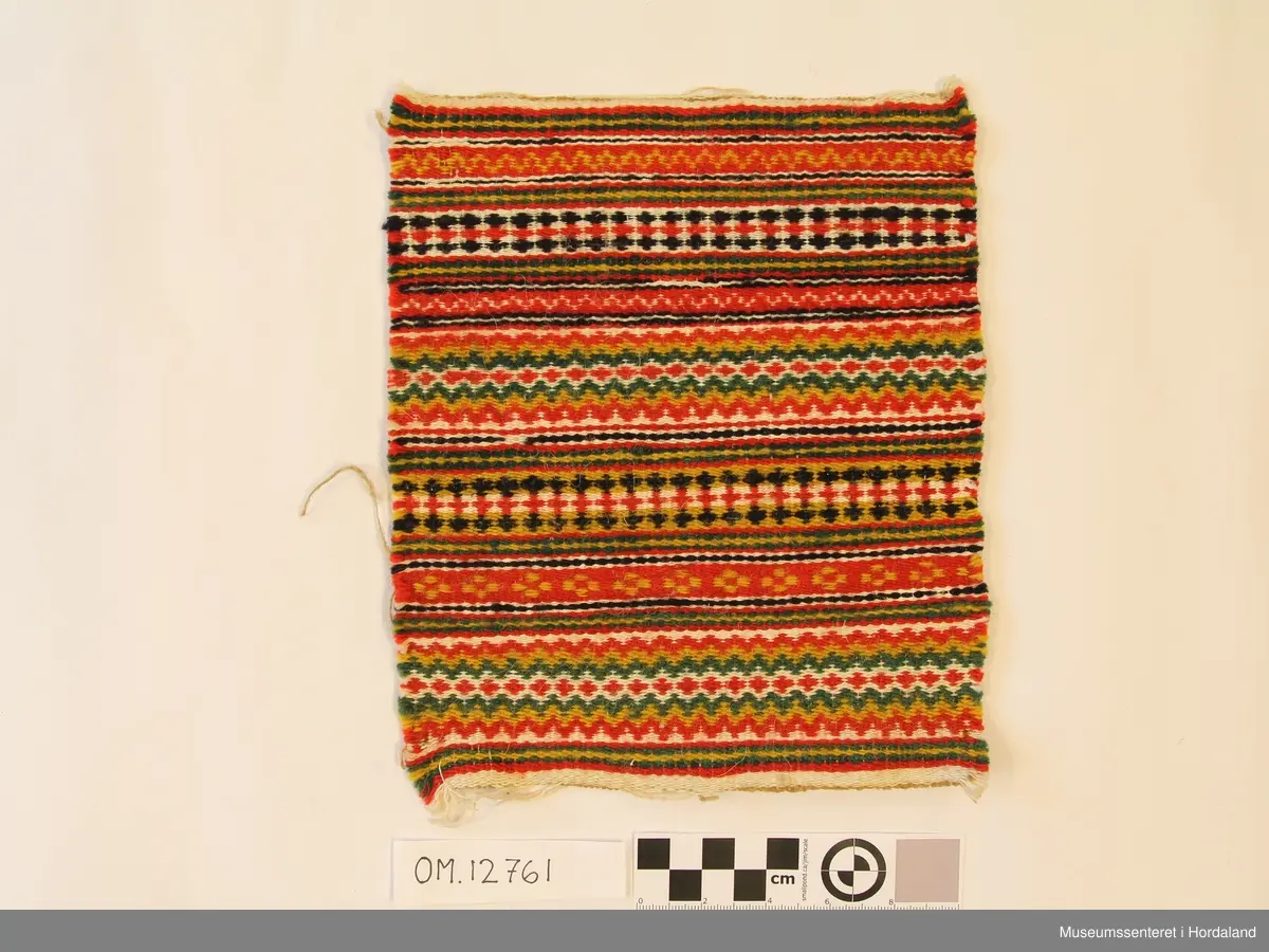 Bringklut voven i krokbrgd teknikk. Mønsteret er i border på tvers. Vevd i ullgarn og lingarn.  Bringkluten er klipt ut av eit større stykke. Ikkje montert på noko stoff.