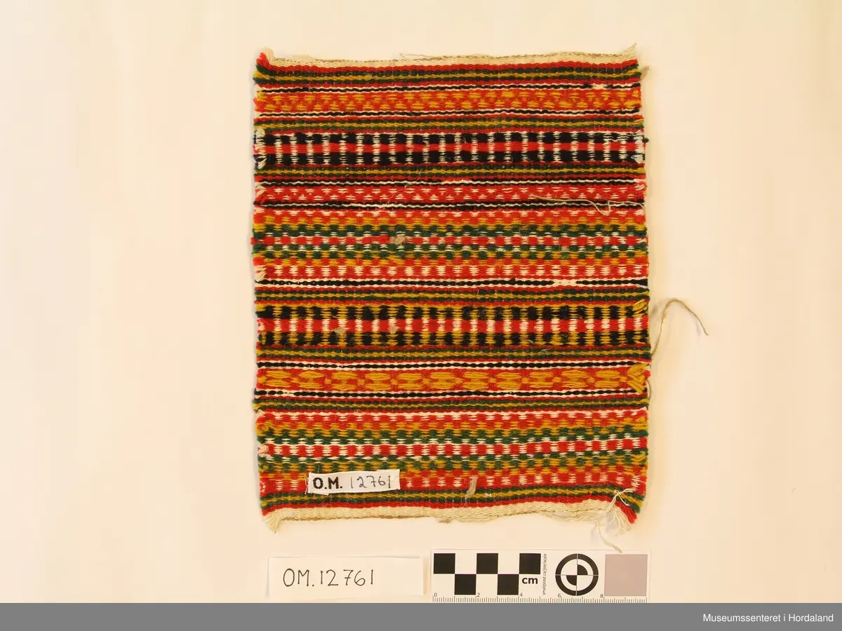 Bringklut voven i krokbrgd teknikk. Mønsteret er i border på tvers. Vevd i ullgarn og lingarn.  Bringkluten er klipt ut av eit større stykke. Ikkje montert på noko stoff.