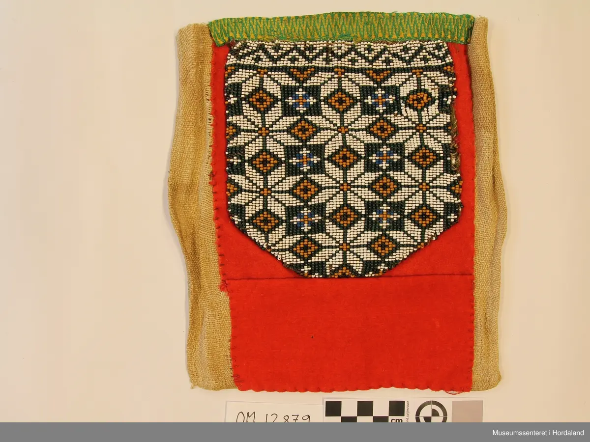 Rektangulær perle-brystduk med påsydd perlenett på raudt ullstoff. Perlenettet er først  montert på eit anna stoff. Åttebladroser som motiv. Det raude ullstoffet er skjøtt rett nedanfor perleveven.  Krokakvarde oppe i grønt og gult. Bakstykke i naturfarga lin.