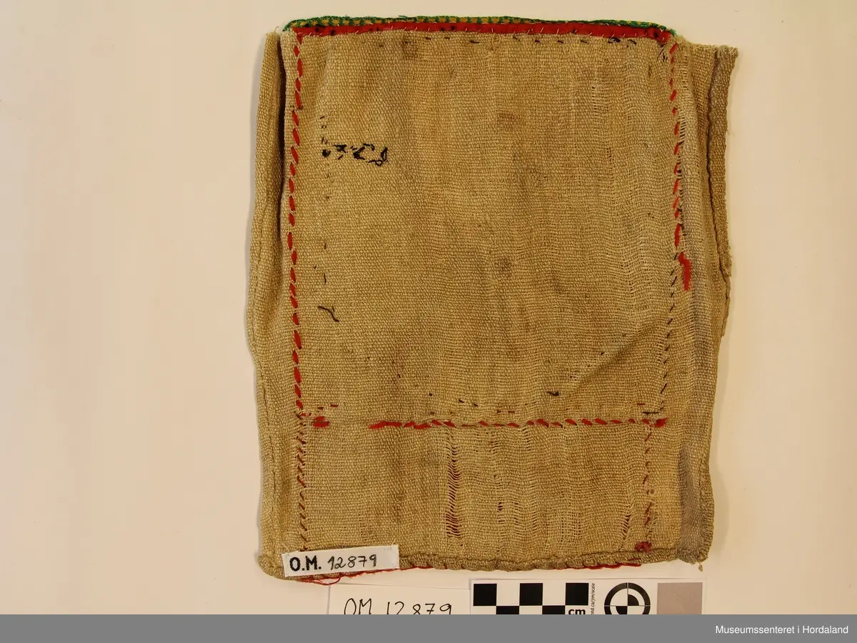 Rektangulær perle-brystduk med påsydd perlenett på raudt ullstoff. Perlenettet er først  montert på eit anna stoff. Åttebladroser som motiv. Det raude ullstoffet er skjøtt rett nedanfor perleveven.  Krokakvarde oppe i grønt og gult. Bakstykke i naturfarga lin.