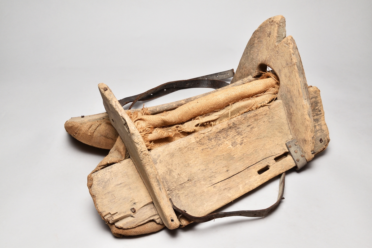 Klövjsadel med sido- och tvärstycken av trä. Mittdelen består av säckväv, stoppad med krollsplint. Båda tvärstyckena (eller valven) har en toppig form, det bakre är avhugget och det främre har ett v-format urtag. Nertill på tvärstyckena finns avlånga hål, troligen för remmar. Fyra korta spännremmar finns fortfarande kvar på sadeln. I bakre tvärstycket finns två hål där det troligen suttit en bygel.