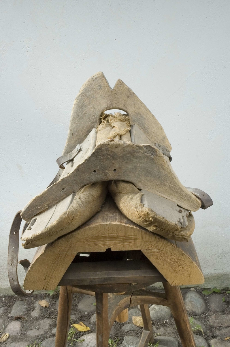 Klövjsadel med sido- och tvärstycken av trä. Mittdelen består av säckväv, stoppad med krollsplint. Båda tvärstyckena (eller valven) har en toppig form, det bakre är avhugget och det främre har ett v-format urtag. Nertill på tvärstyckena finns avlånga hål, troligen för remmar. Fyra korta spännremmar finns fortfarande kvar på sadeln. I bakre tvärstycket finns två hål där det troligen suttit en bygel.