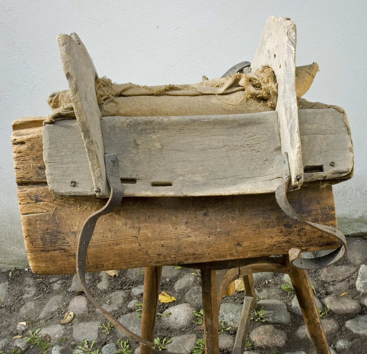 Klövjsadel med sido- och tvärstycken av trä. Mittdelen består av säckväv, stoppad med krollsplint. Båda tvärstyckena (eller valven) har en toppig form, det bakre är avhugget och det främre har ett v-format urtag. Nertill på tvärstyckena finns avlånga hål, troligen för remmar. Fyra korta spännremmar finns fortfarande kvar på sadeln. I bakre tvärstycket finns två hål där det troligen suttit en bygel.