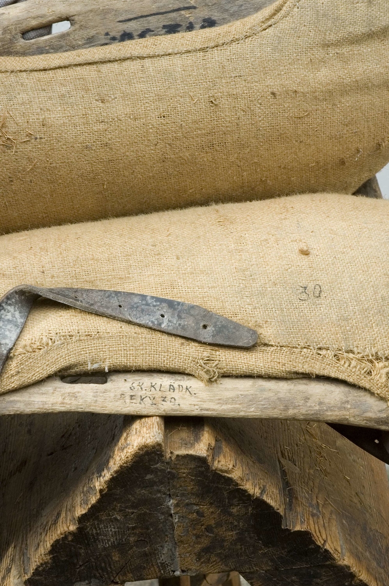 Klövjsadel med sido- och tvärstycken av trä. Mittdelen består av säckväv, stoppad med krollsplint. Båda tvärstyckena (eller valven) har en toppig form, det bakre är avhugget och det främre har ett v-format urtag. Nertill på tvärstyckena finns avlånga hål, troligen för remmar. Fyra korta spännremmar finns fortfarande kvar på sadeln. I bakre tvärstycket finns två hål där det troligen suttit en bygel.
