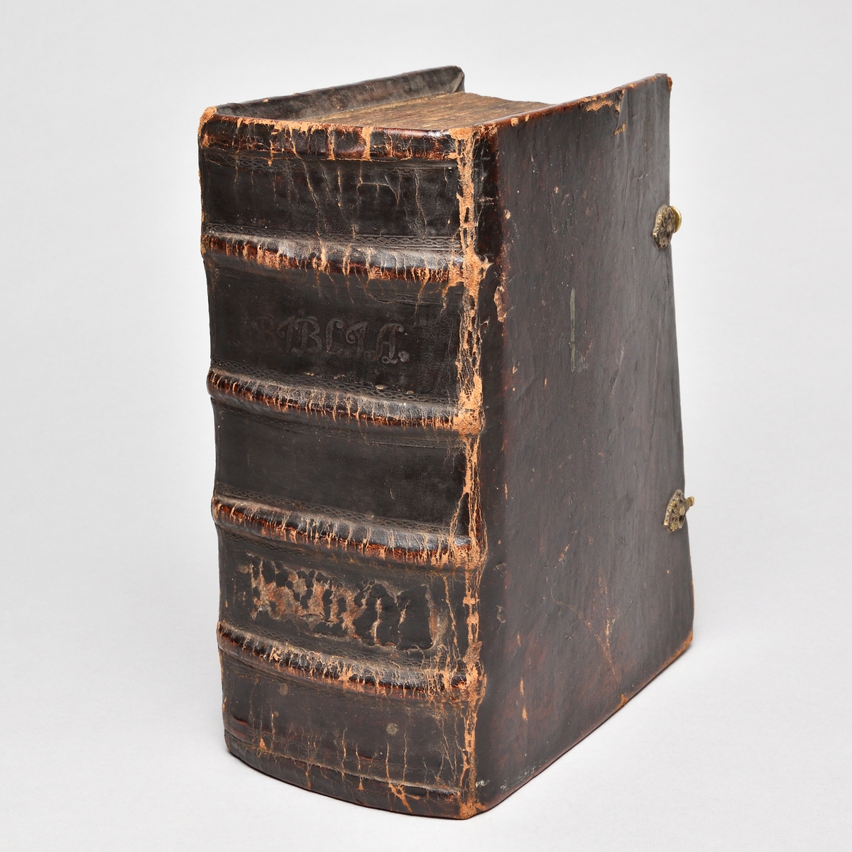 Bibel med band av skinn, rygg med fyra upphöjda bind. Två bokspännen av skinn och mässingsknäppen.