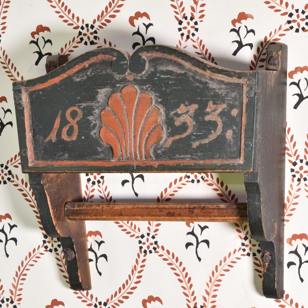 Handklähylla av furu, målad mörkgrön. Formad som en öppen låda med sidor och botten. Förlängda sidogavlar, nedtill profilerade, med instucken hängstång. Framsidan med snidad rocaillesnäcka i rött samt årtalet "1833".