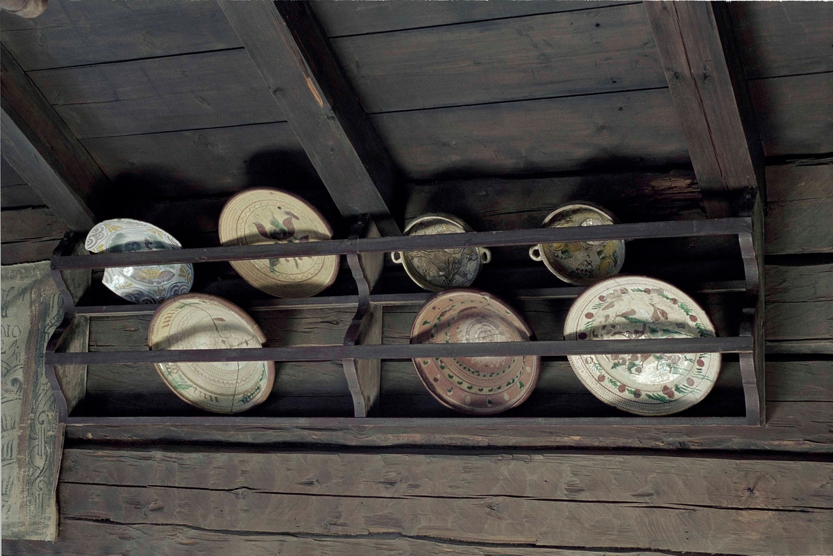 Kärlhylla av furu, brunmålad, långsmal med två hyllplan, profilerade gavlar samt mittpost. Två längsgående lister håller kärlen på plats.