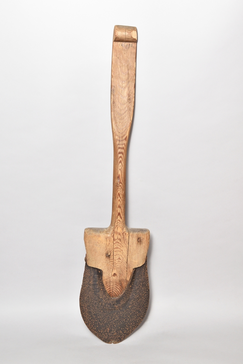 Spade, av furu, järnskodd till ungefär halva bladet. Skaftet bredare uppåt, avslutat med en handvalk.
