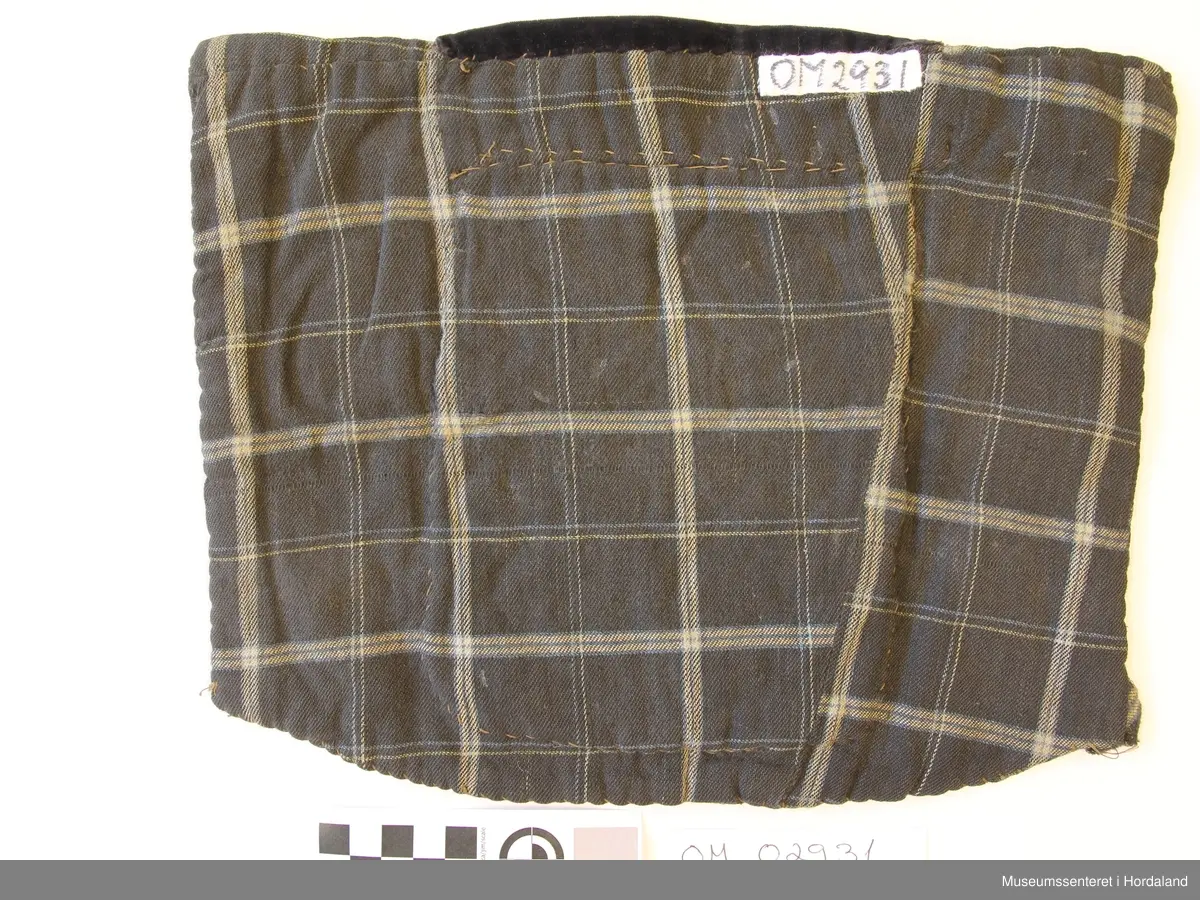 Rektangulær brystduk som er brodert i kross-sting (halve og heile). Åtteblad-rose som hovudmotiv og ruter. Broderiet er litt slitt. Svart fløyelsband oppe. Broderiet er sydd på linstoff. Bakstykket og sidestykke er i bomull - rutete mønster.