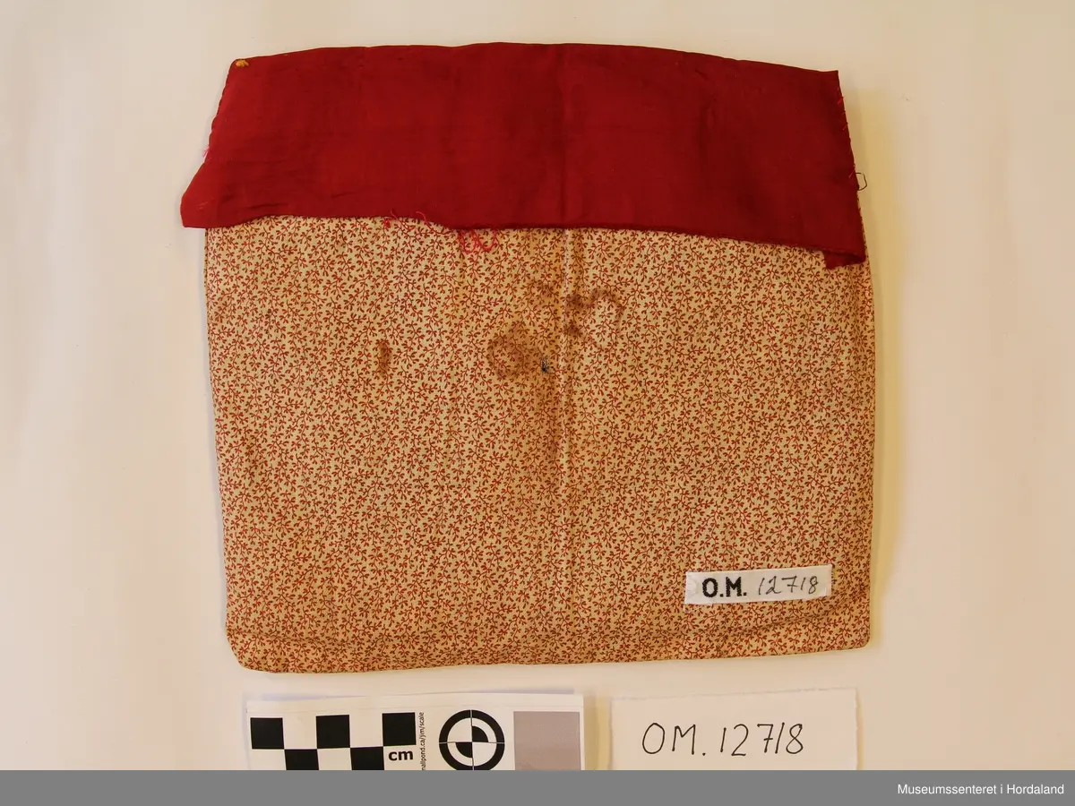 Kvadratisk bringeduk med perlemotiv med stråperler montert på svart fløyel - 3 åttebladroser. Overfor perlemotivet er det raud silkekant med gullband utanpå. Alt er montert på eit småmønstra bomullstoff som ligg som ei "lomme"  - inni "lomma" ligg eit tjukt mellomfõr.