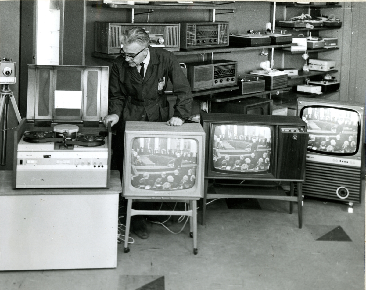 Olaf T. Ranum i  butikken i Oalv Tryggvasonsgate 18, Trondheim. I tv og radio avdelingen. Ranum ser på en båndopptaker. Tv-sending på tre tver. Radioer og grammofoner i hyller i bakgrunnen.